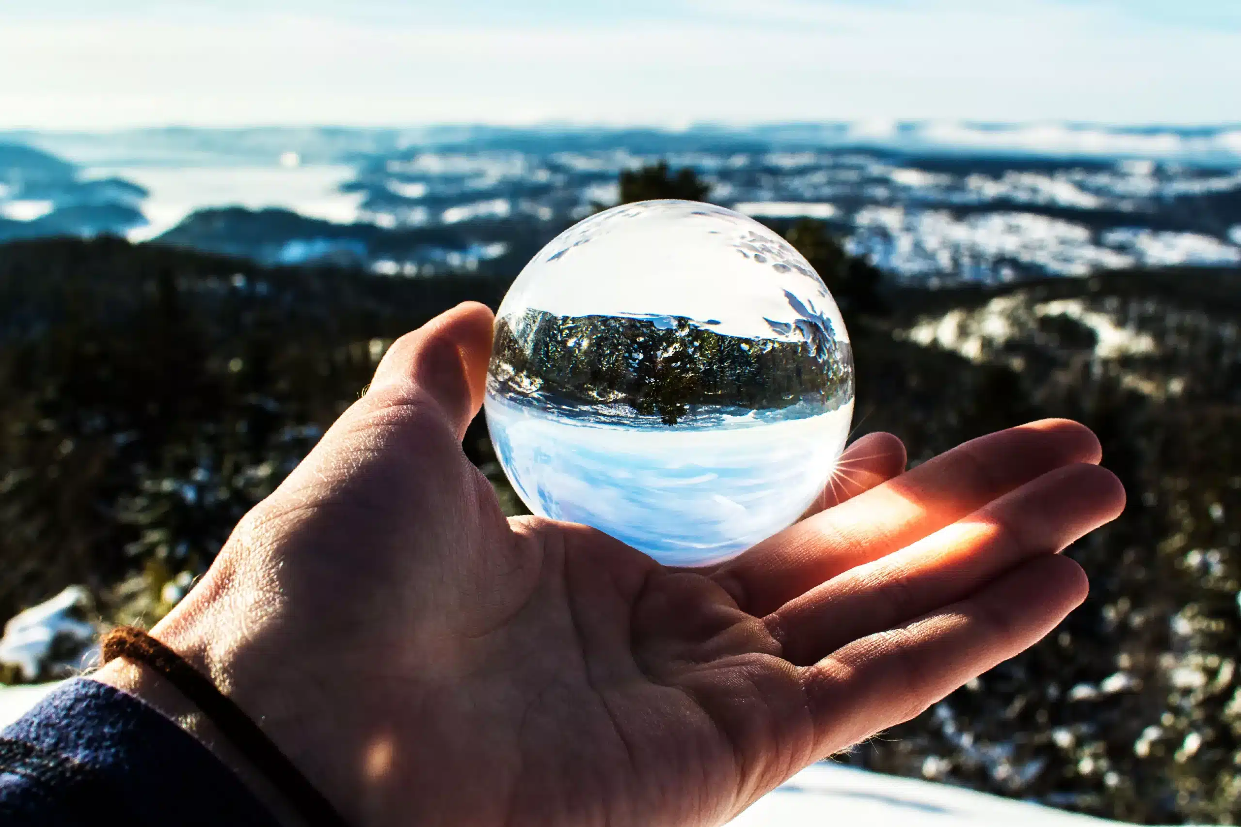 A hand holding a glass sphere up to a wide landscape, the view turned upside down inside it