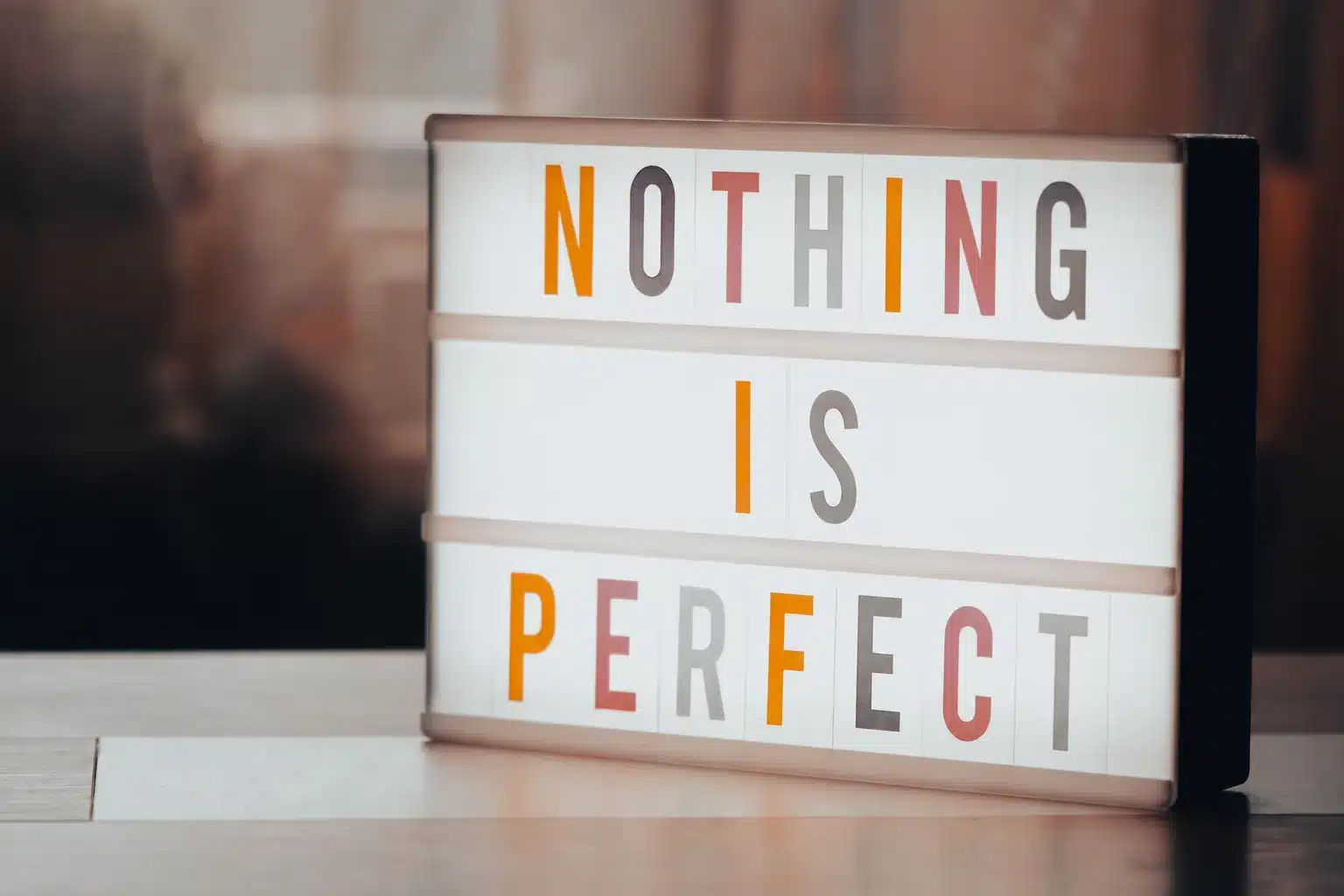 Illuminated sign with colourful letters reading “NOTHING IS PERFECT”.