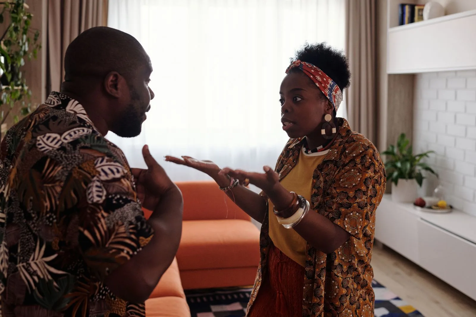 A man and a woman in their living room in the middle of a heated disagreement, both gesturing.