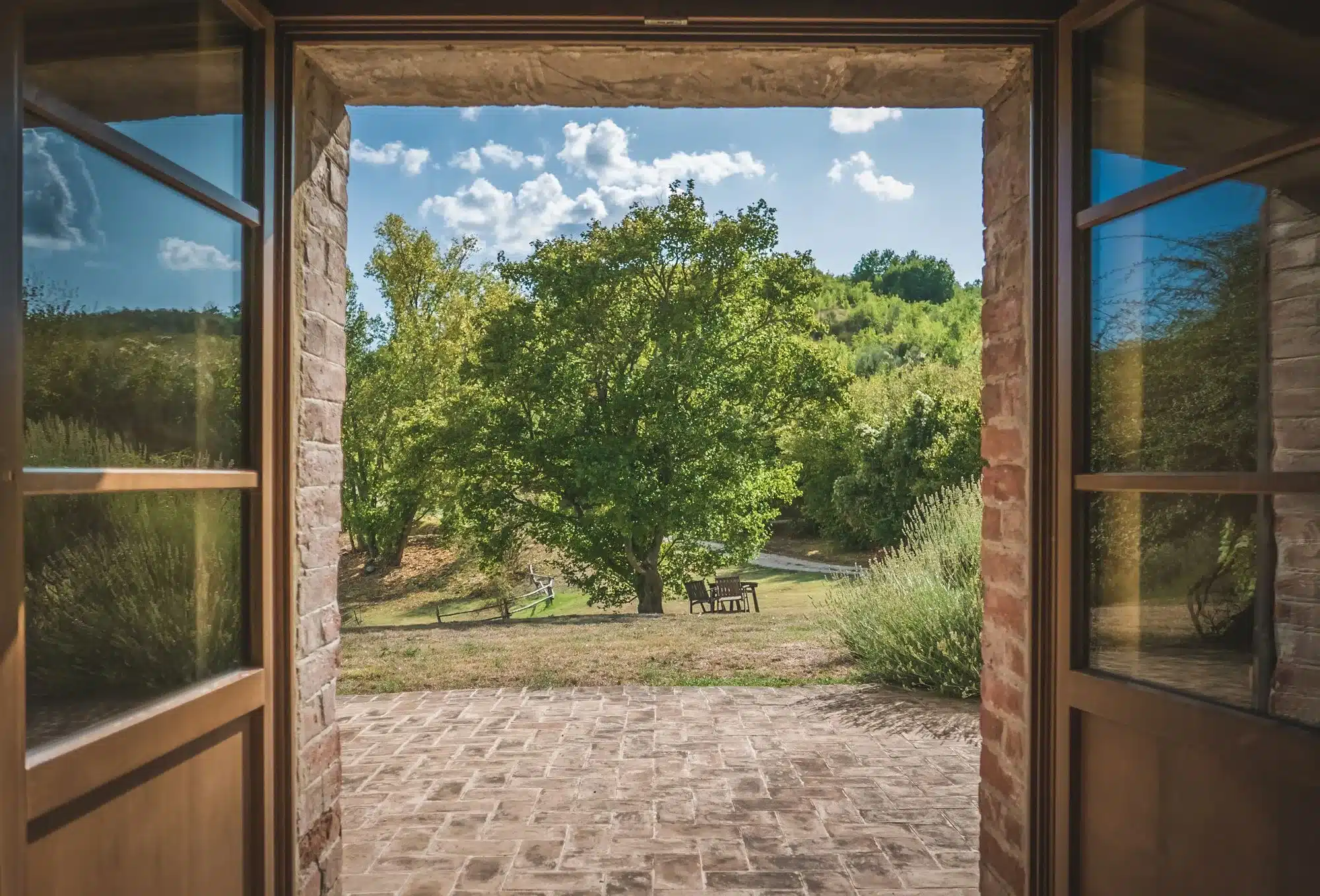 A dark stone doorway opening onto a bright, green Italian landscape under a blue sky