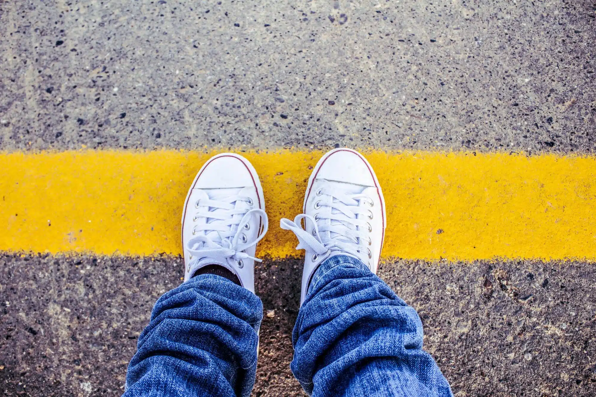 White trainers standing on grey tarmac just behind a painted yellow line