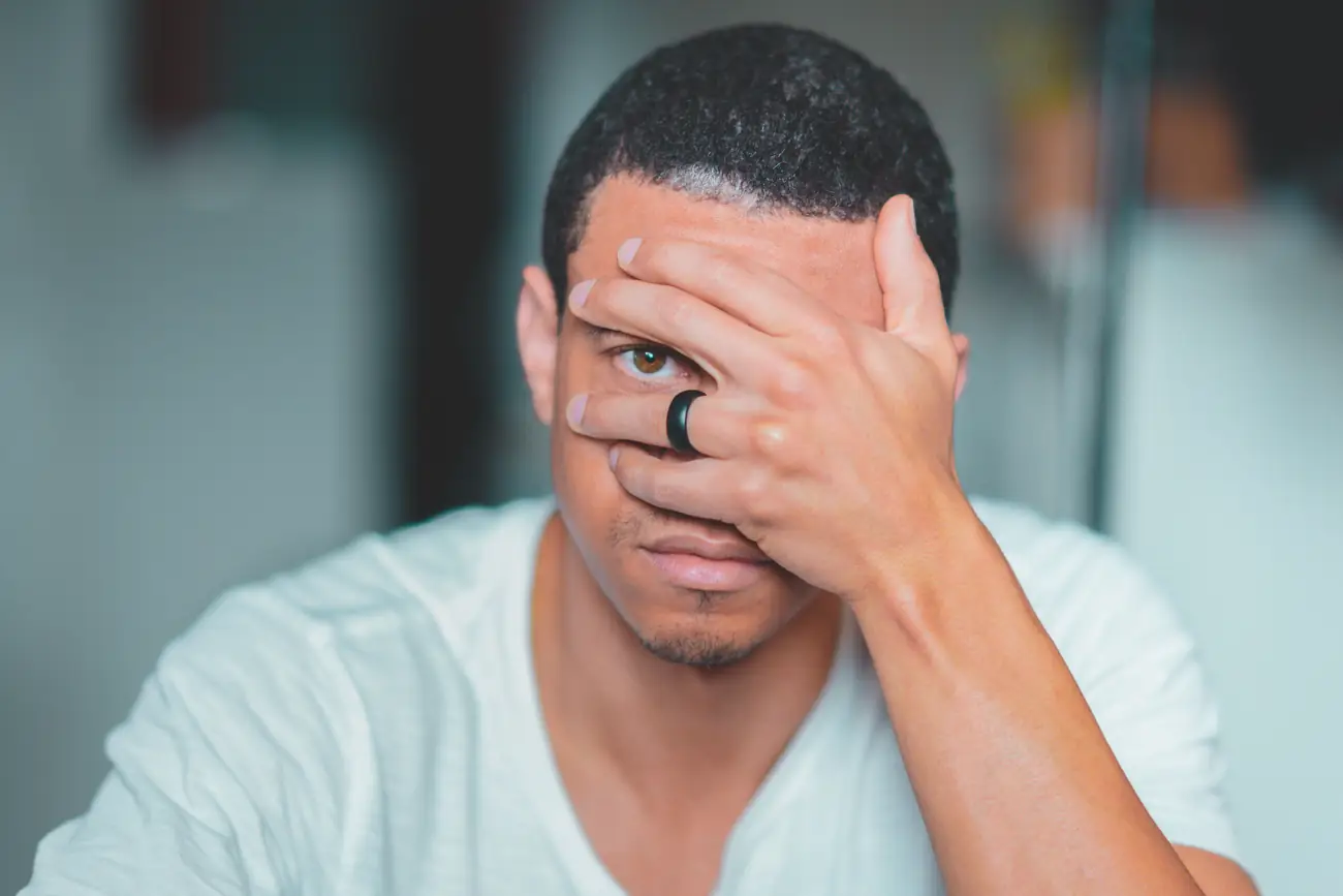A man sitting with one hand over his face, looking out through his fingers