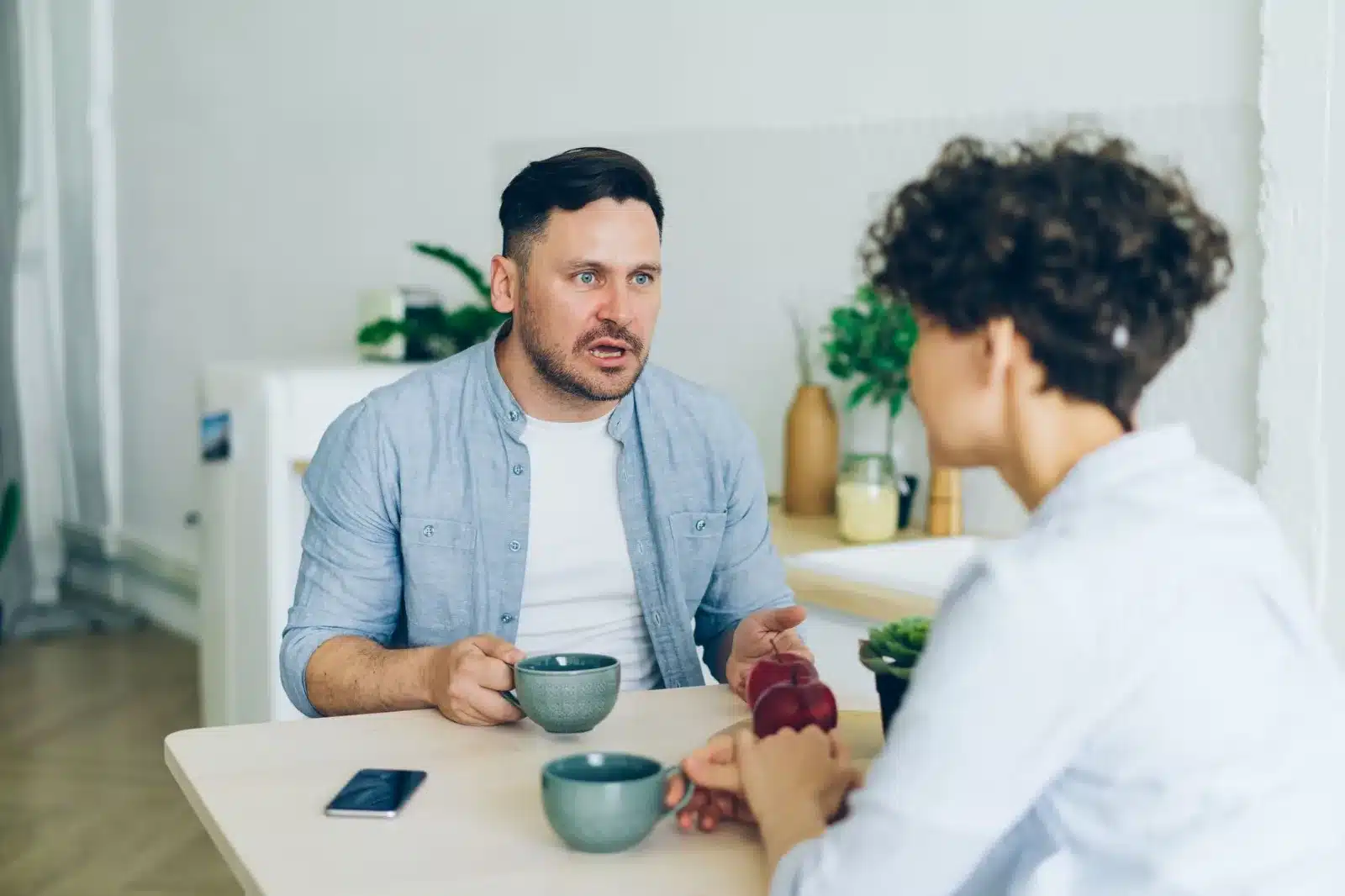 Two adults having a serious conversation at a kitchen table.
