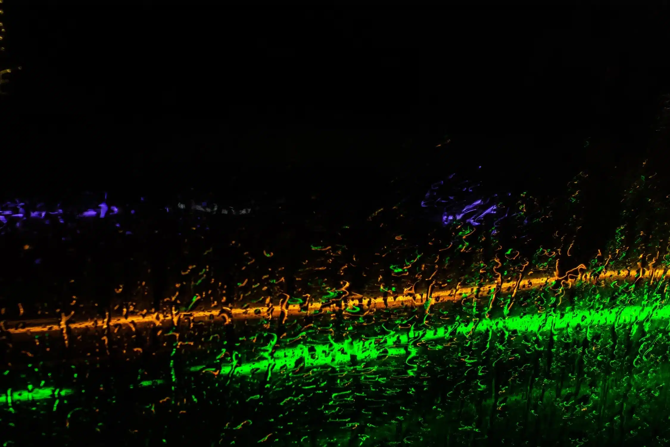 Abstract green, amber and purple light reflected through water droplets on glass against a dark background.