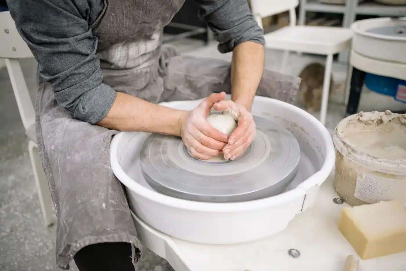 Hands shaping a small clay pot on a pottery wheel in a studio.