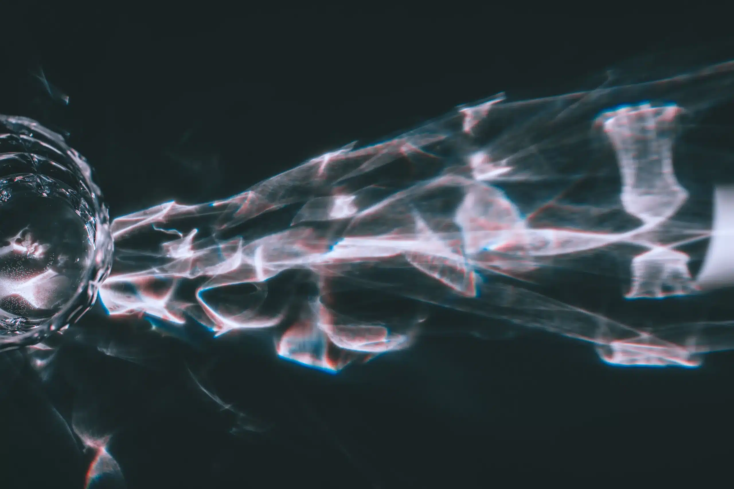 Pale blue and rose light refracted through faceted glass across a dark surface.